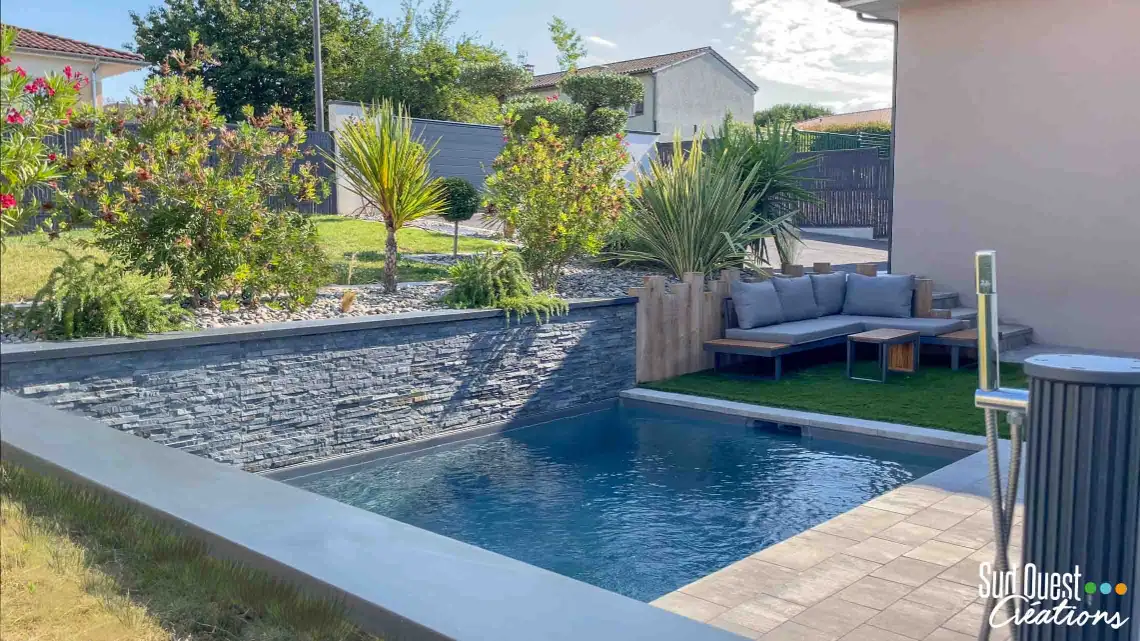 Piscine paysagère de 4x2.5m avec liner sable donnant une eau vert d'eau, intégrée dans un décor de rocailles et plantes exotiques à Castanet-Tolosan, Haute-Garonne.