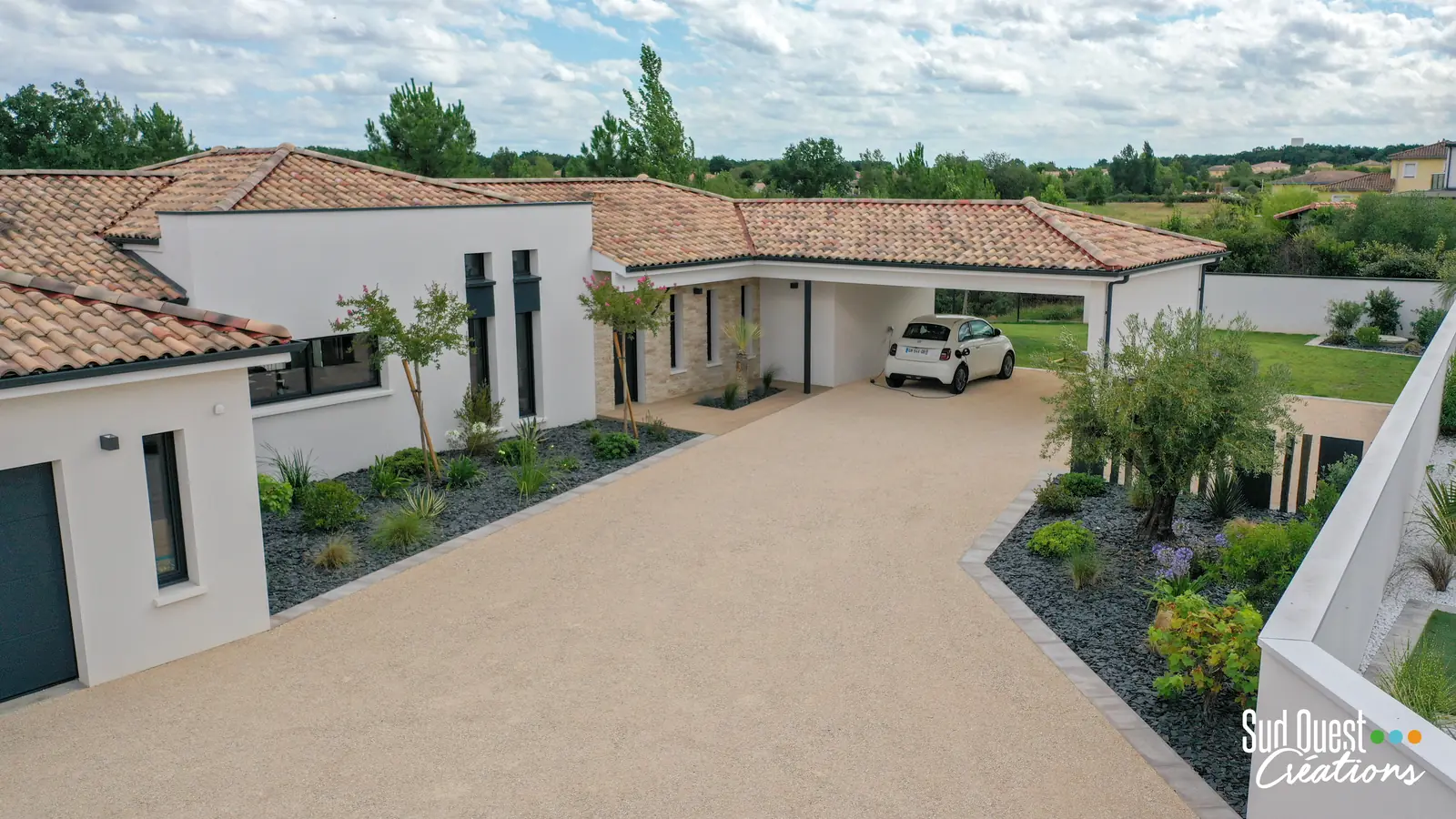 Allée carrossable en gravillons bordée de massifs d'ardoise et d'un olivier