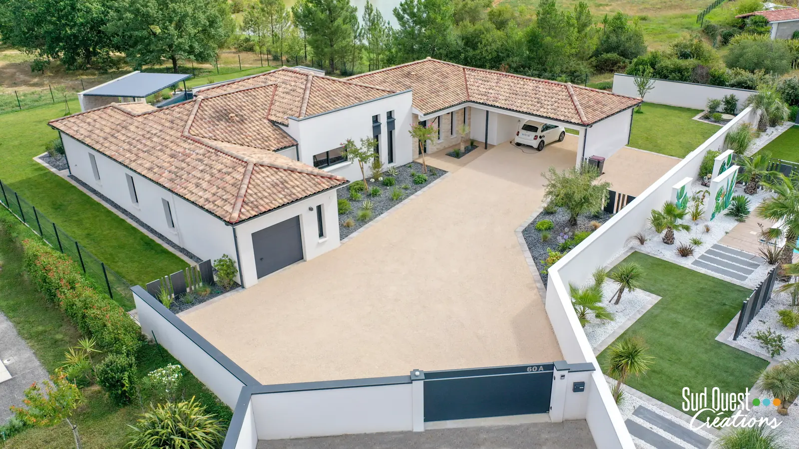 Vue drone d'un aménagement extérieur complet : allée en gravillons, massifs, carport et portail