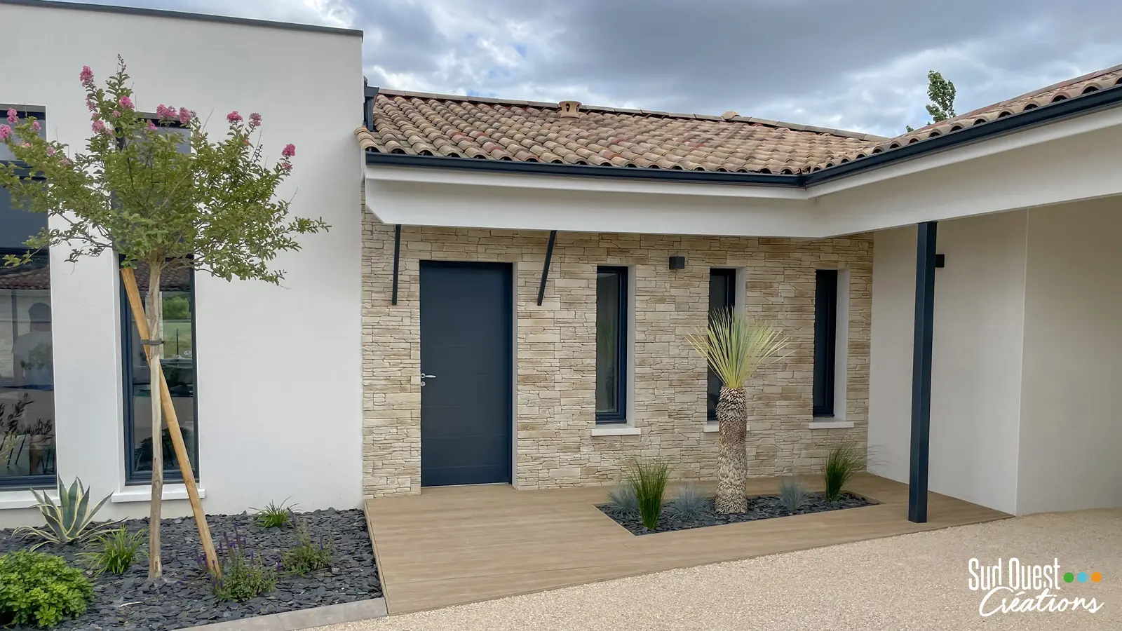 Entrée de maison avec terrasse composite, yucca rostrata et massif d'ardoise