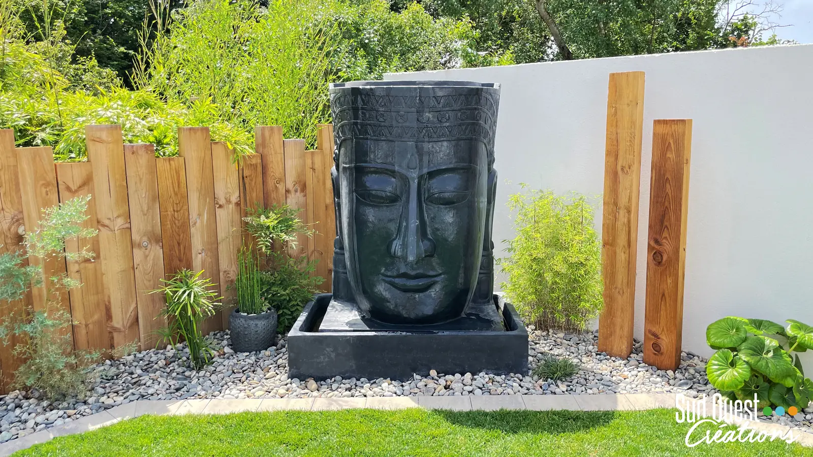 Fontaine tête de Bouddha sur lit de galets, clôture en bois brut, poteaux bois et bambous