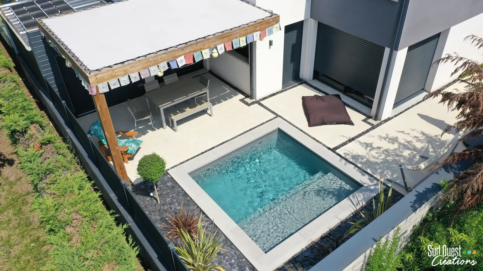 Vue drone d'une mini piscine avec banquette, pergola bois à toile et terrasse en béton désactivé