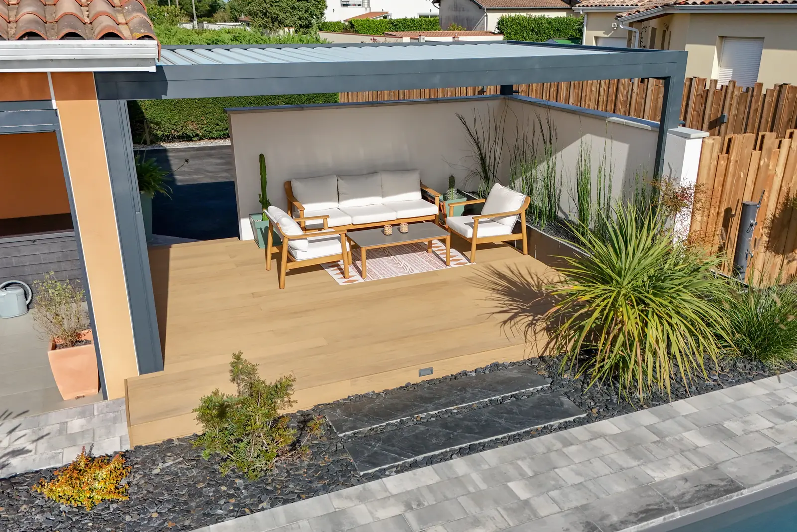 Pergola bioclimatique aluminium sur terrasse bois avec salon extérieur et pas japonais en ardoise