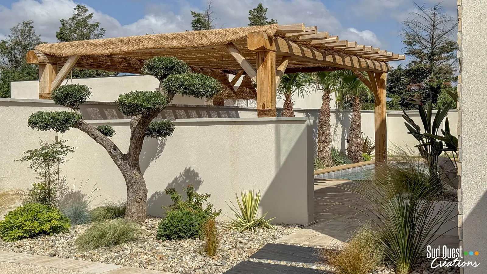 Pergola en bois brut et olivier taillé en nuage dans un massif de galets