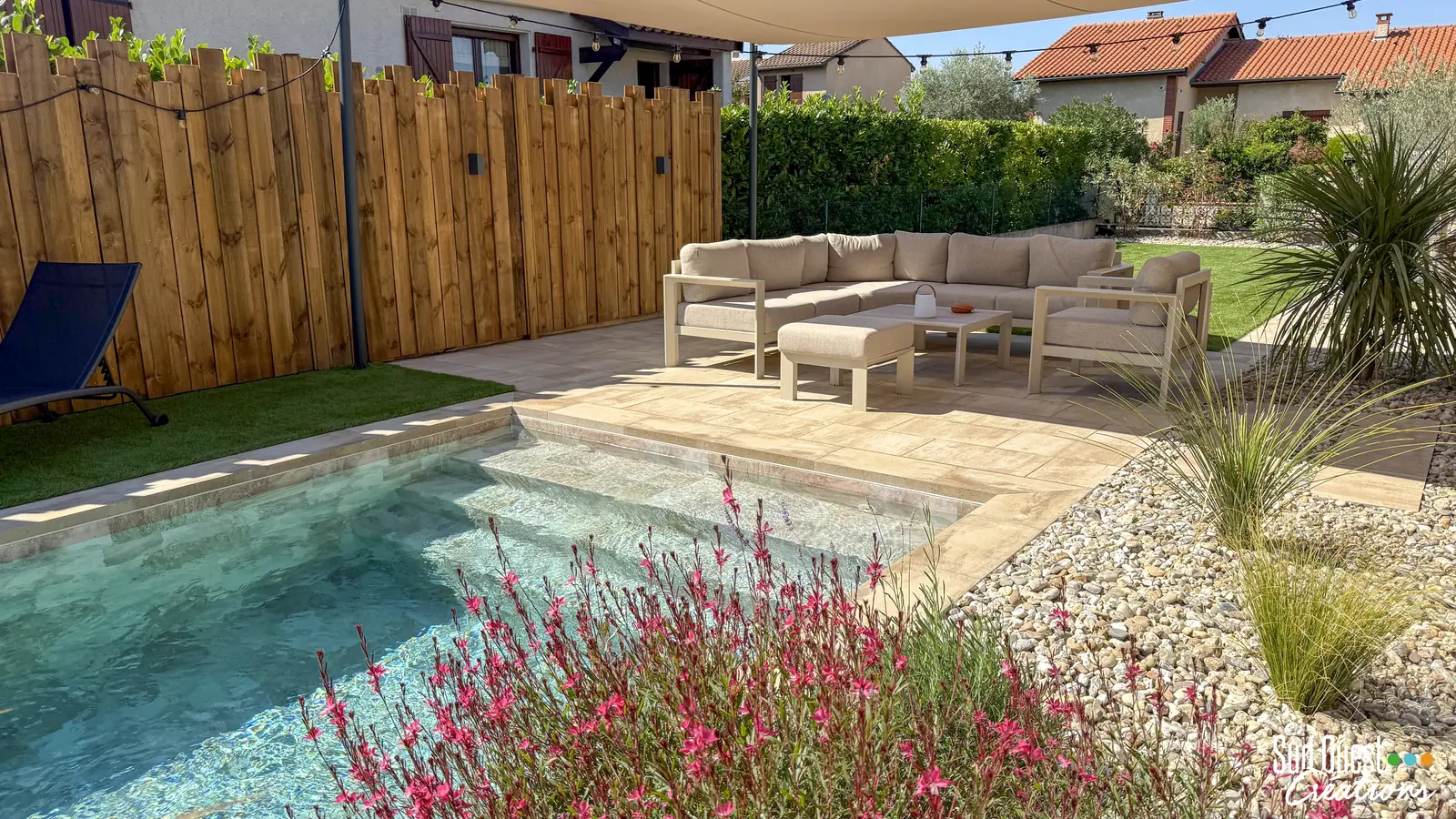 Petite piscine carrelée avec escalier, plage en dallage beige, gauras en fleurs et salon sous voile d'ombrage