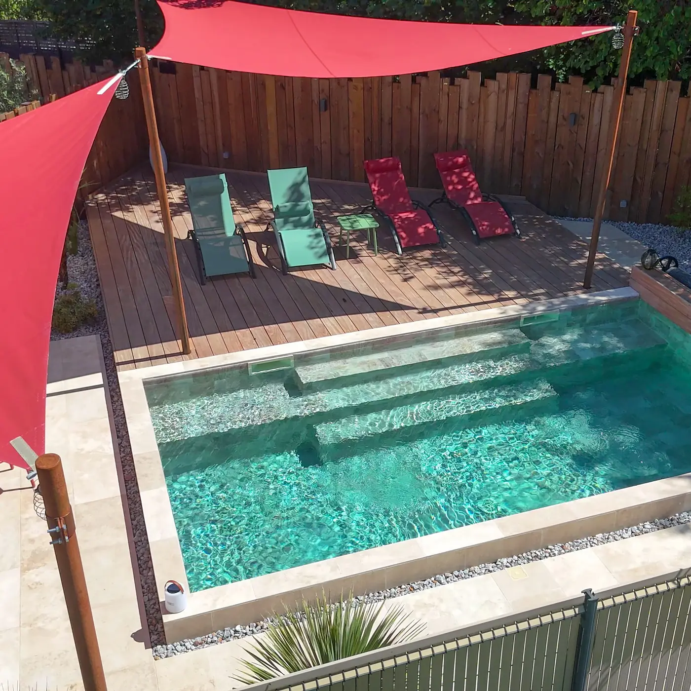 Petite piscine carrelée avec escalier et banquette immergée sous une voile d'ombrage