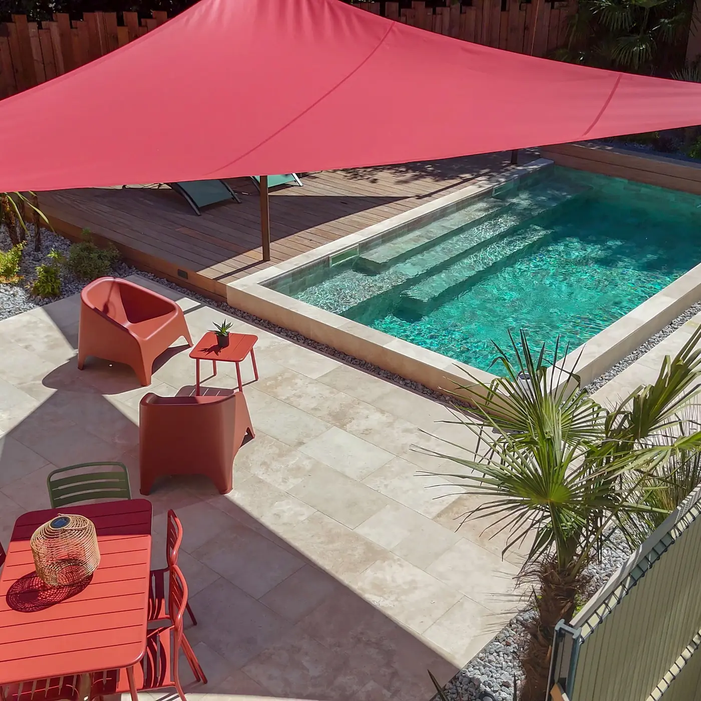 Petite piscine avec plage en travertin, salon de jardin et voile d'ombrage