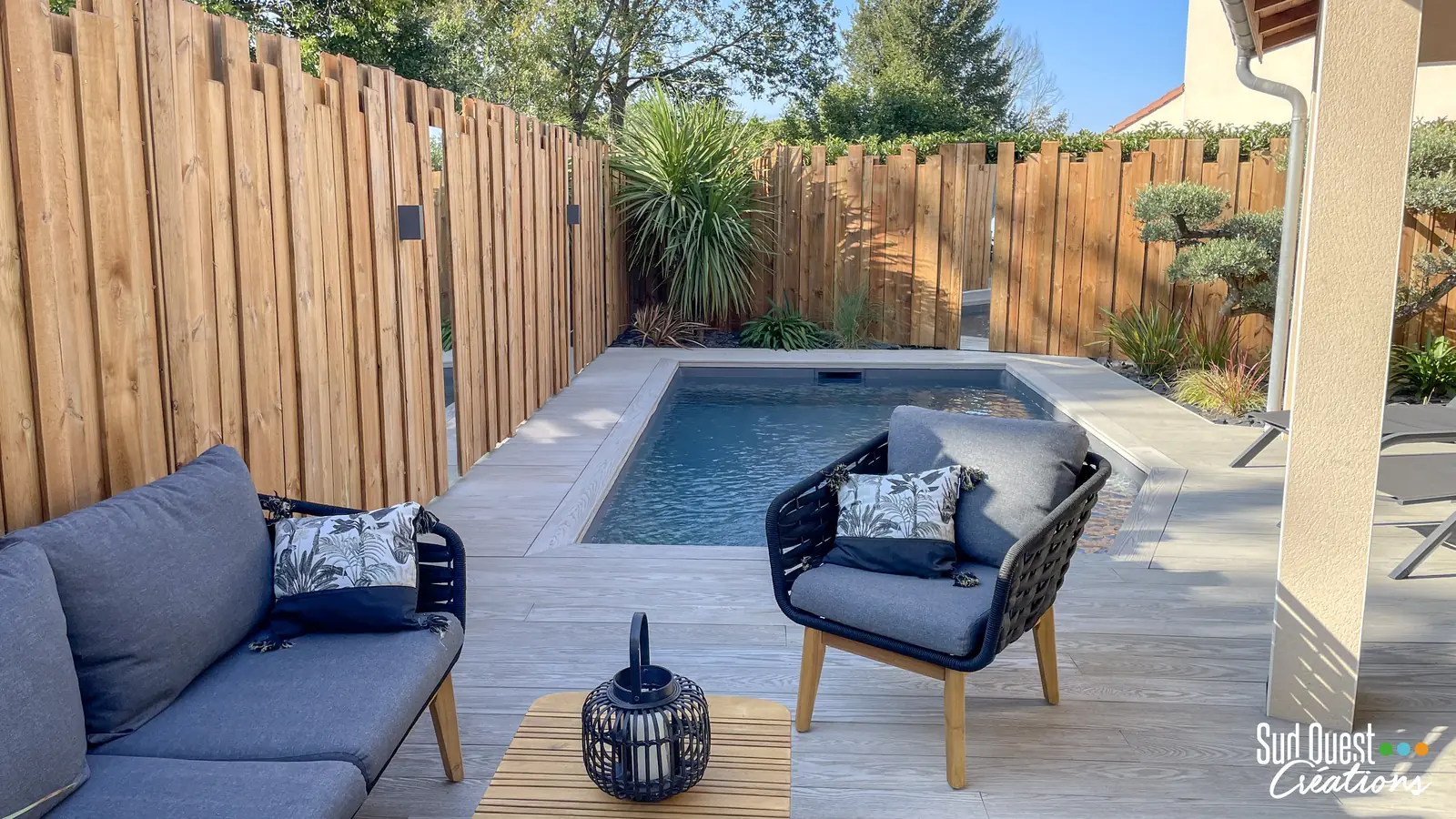 Salon extérieur sur terrasse composite face à une petite piscine, clôture en bois brut