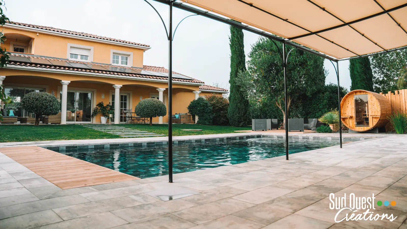 Piscine carrelée devant la maison, pergola métal à toile et sauna tonneau