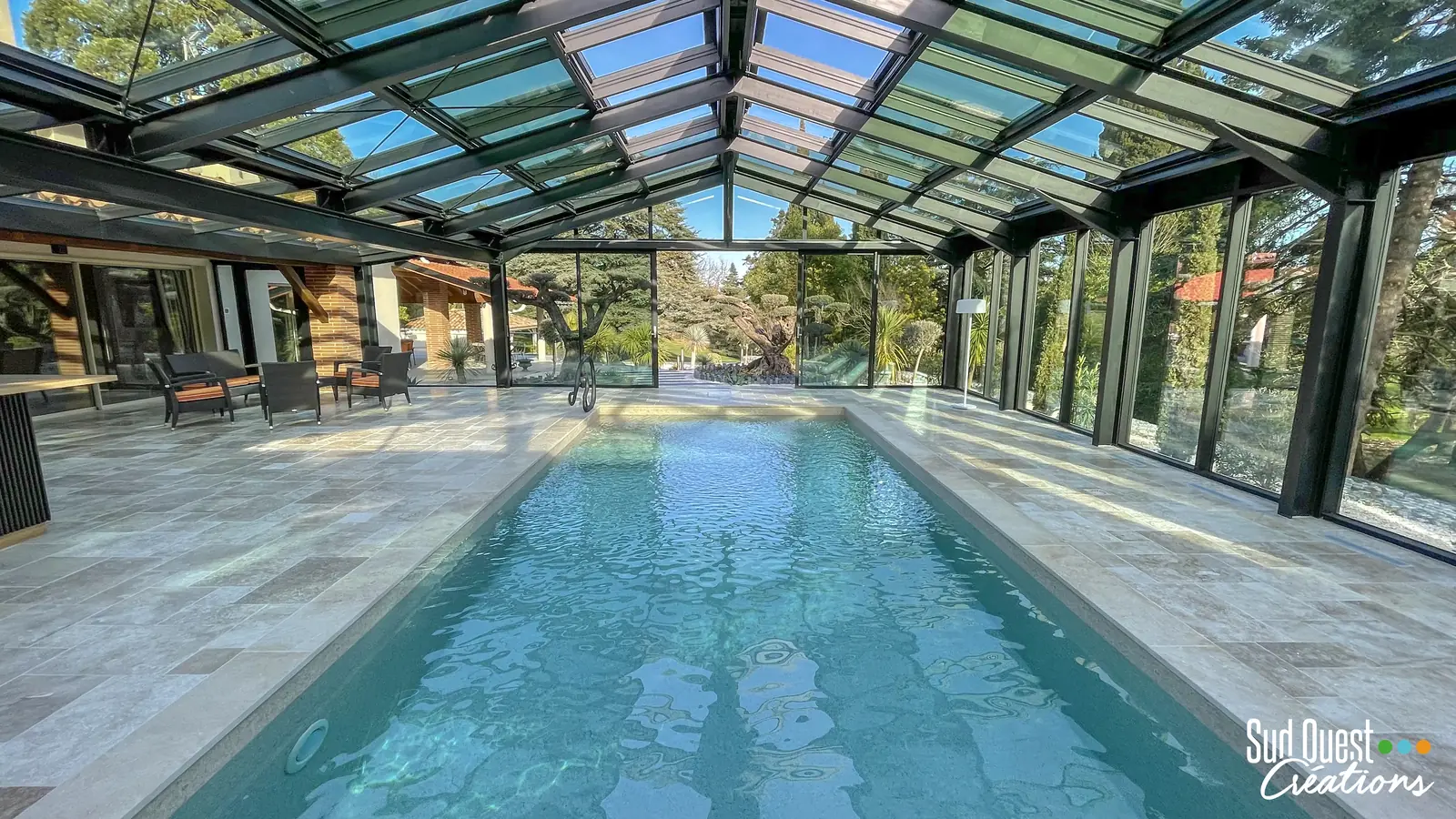 Piscine couverte sous verrière, plage en travertin et salon