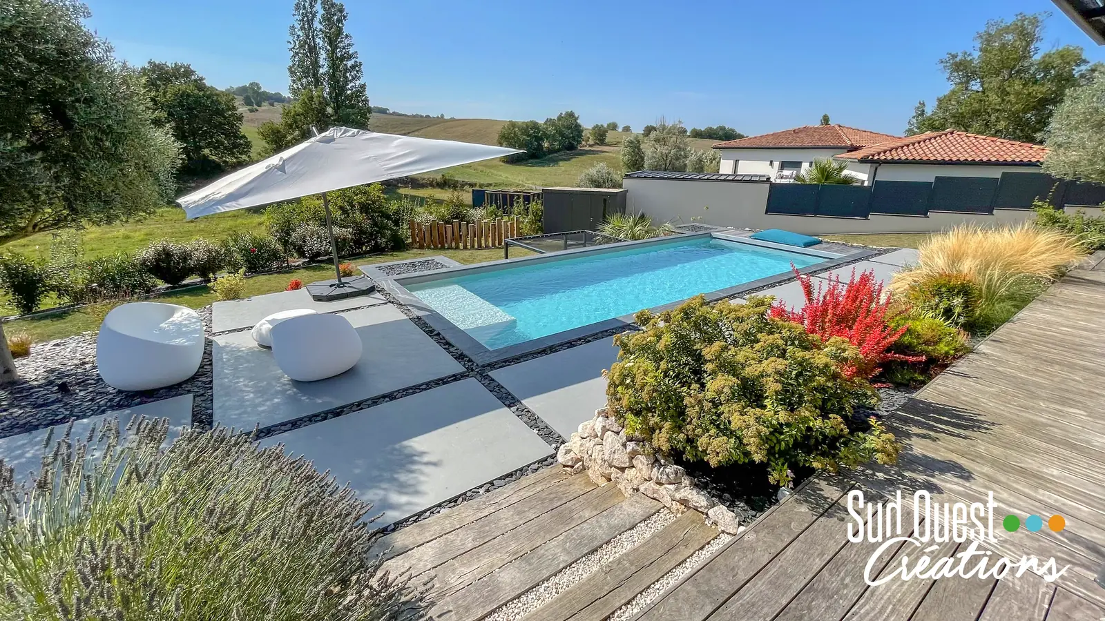 Piscine allongée avec plage en dalles grand format, terrasse bois et vue sur la campagne