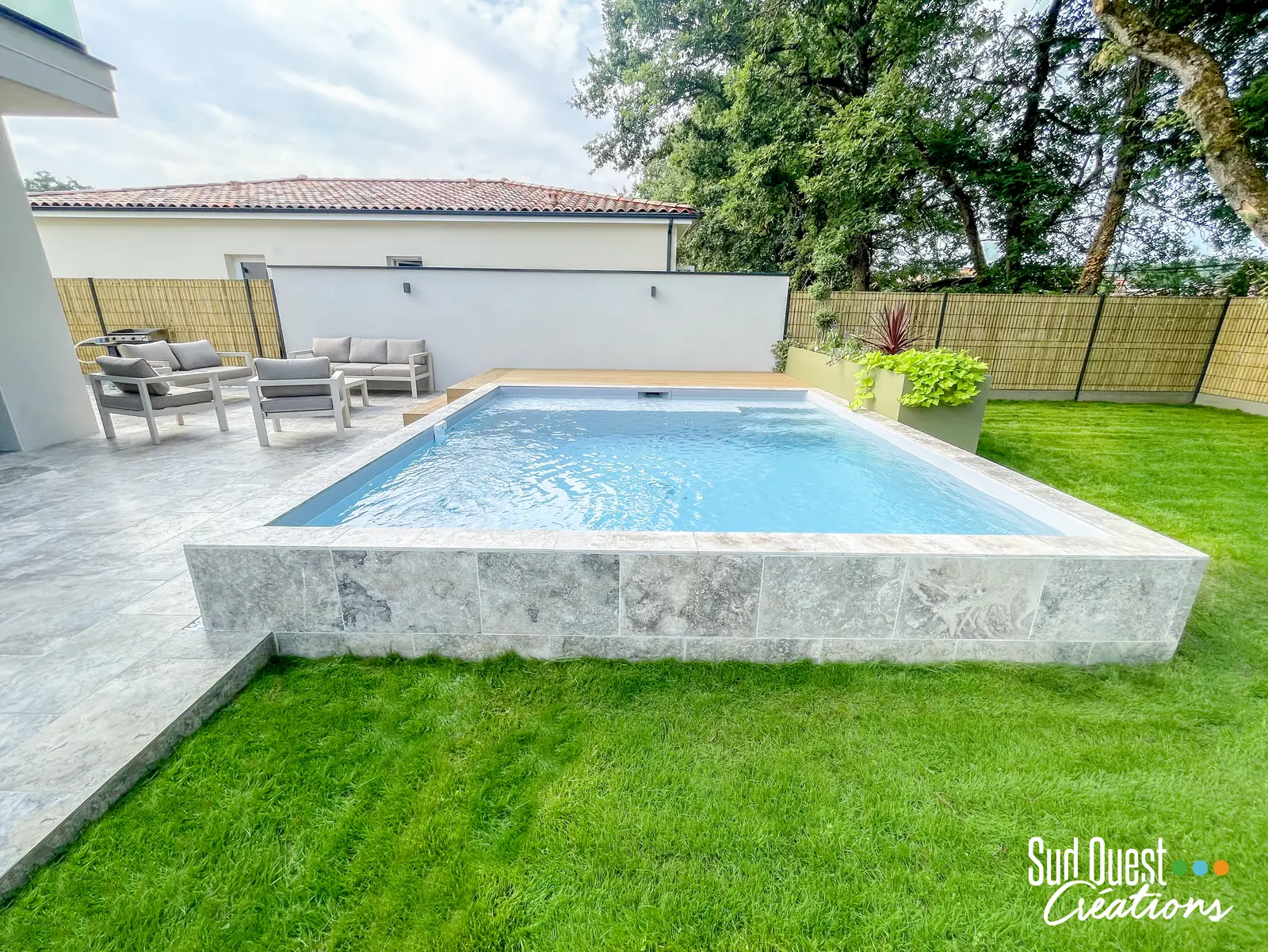 Piscine hors-sol maçonnée habillée de travertin gris, terrasse et pelouse