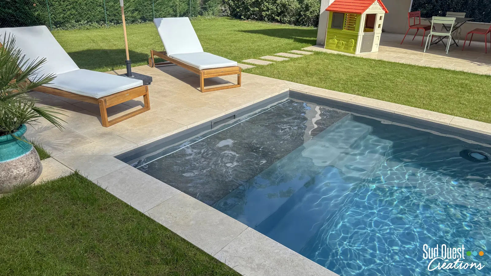 Piscine au liner gris avec banquette immergée, margelles en travertin et pelouse