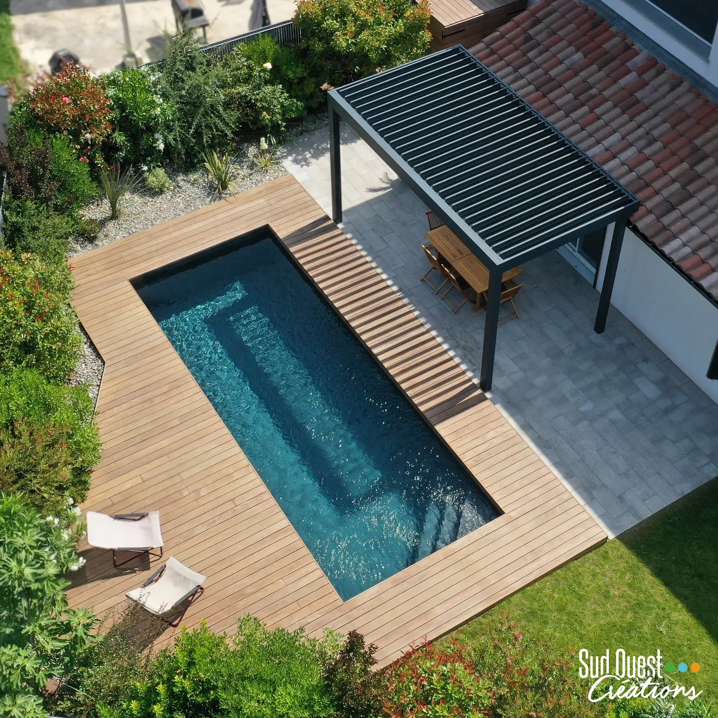 Vue aérienne d'une piscine liner noir entourée d'une terrasse en bois et d'une pergola bioclimatique