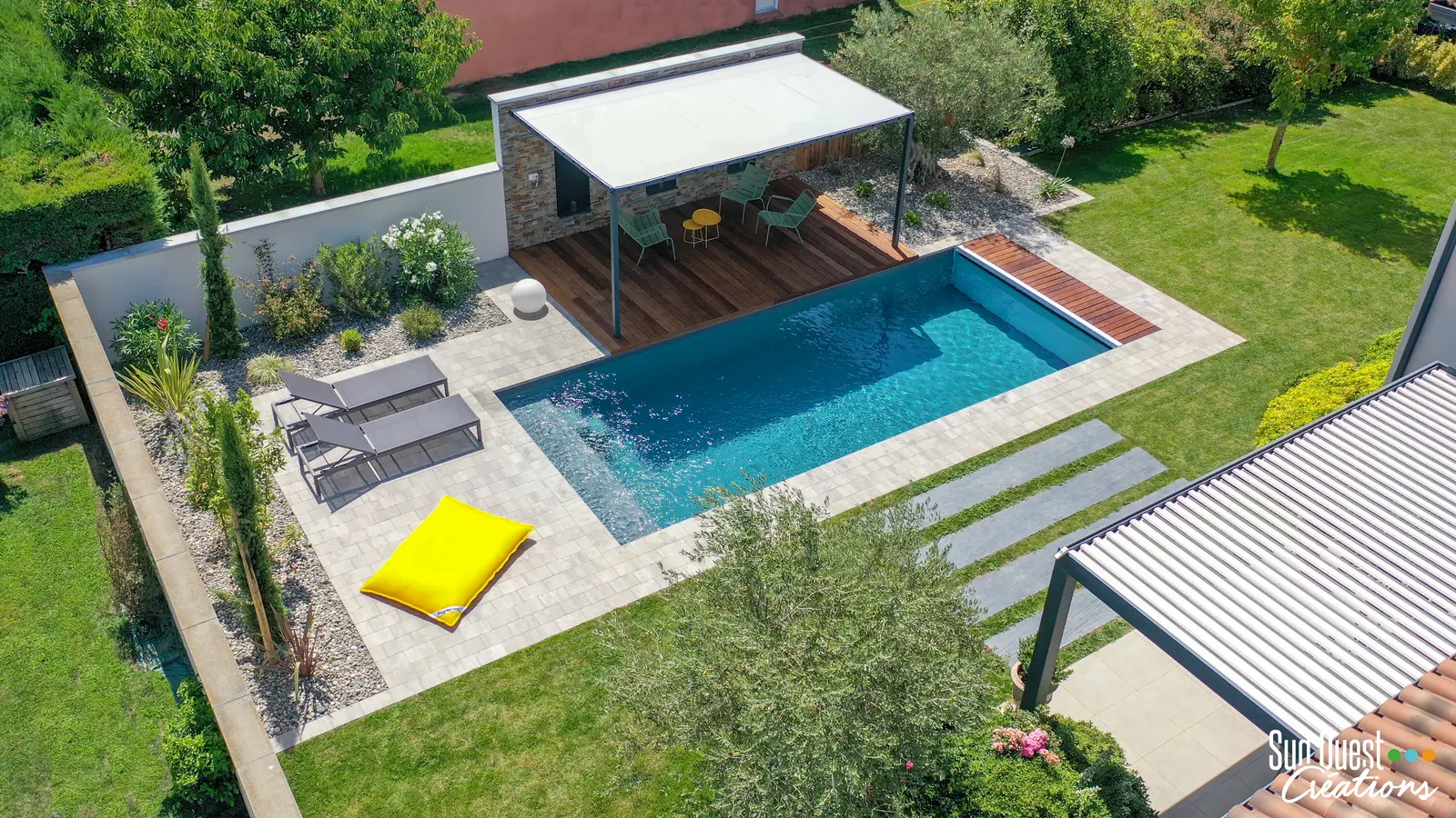 Vue drone d'une piscine avec plage en dallage, pergola bioclimatique, terrasse composite, brasero et palmiers