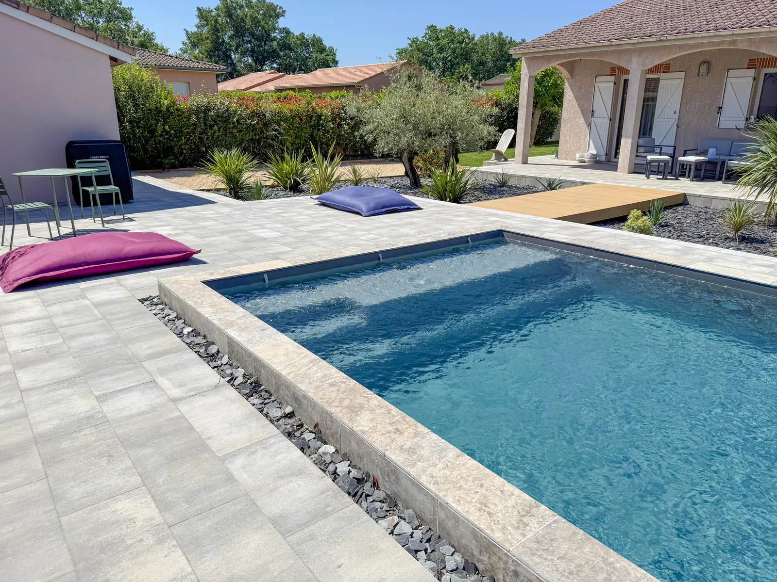 Piscine rectangulaire avec banquette immergée, margelles travertin et plage en dallage gris
