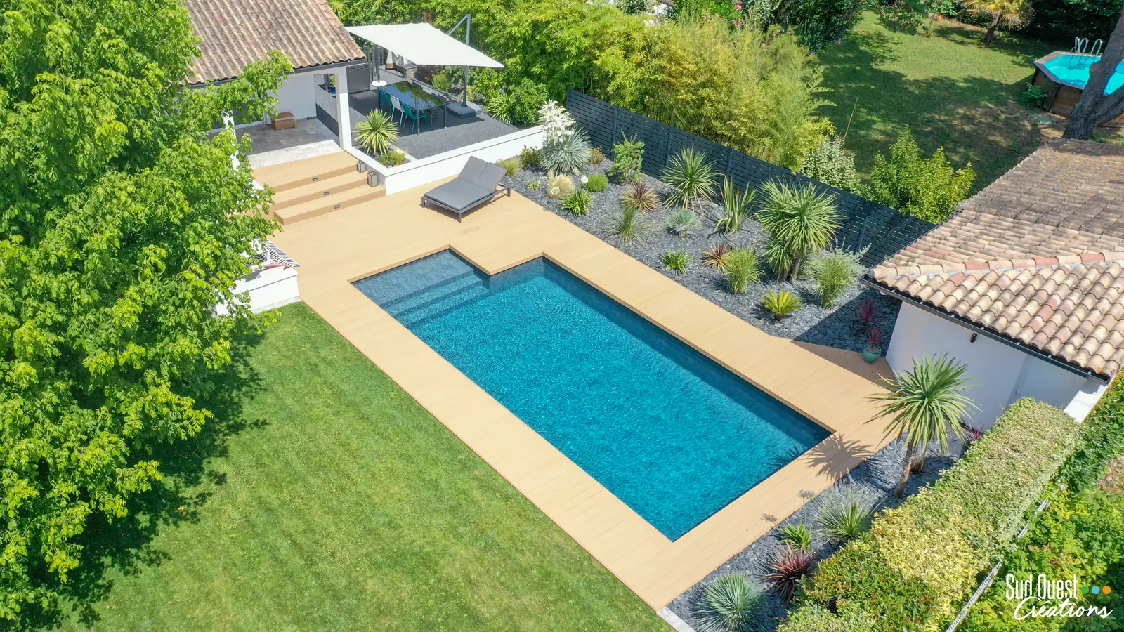 Vue drone d'une piscine entourée de terrasse composite, escaliers et coin repas ombragé