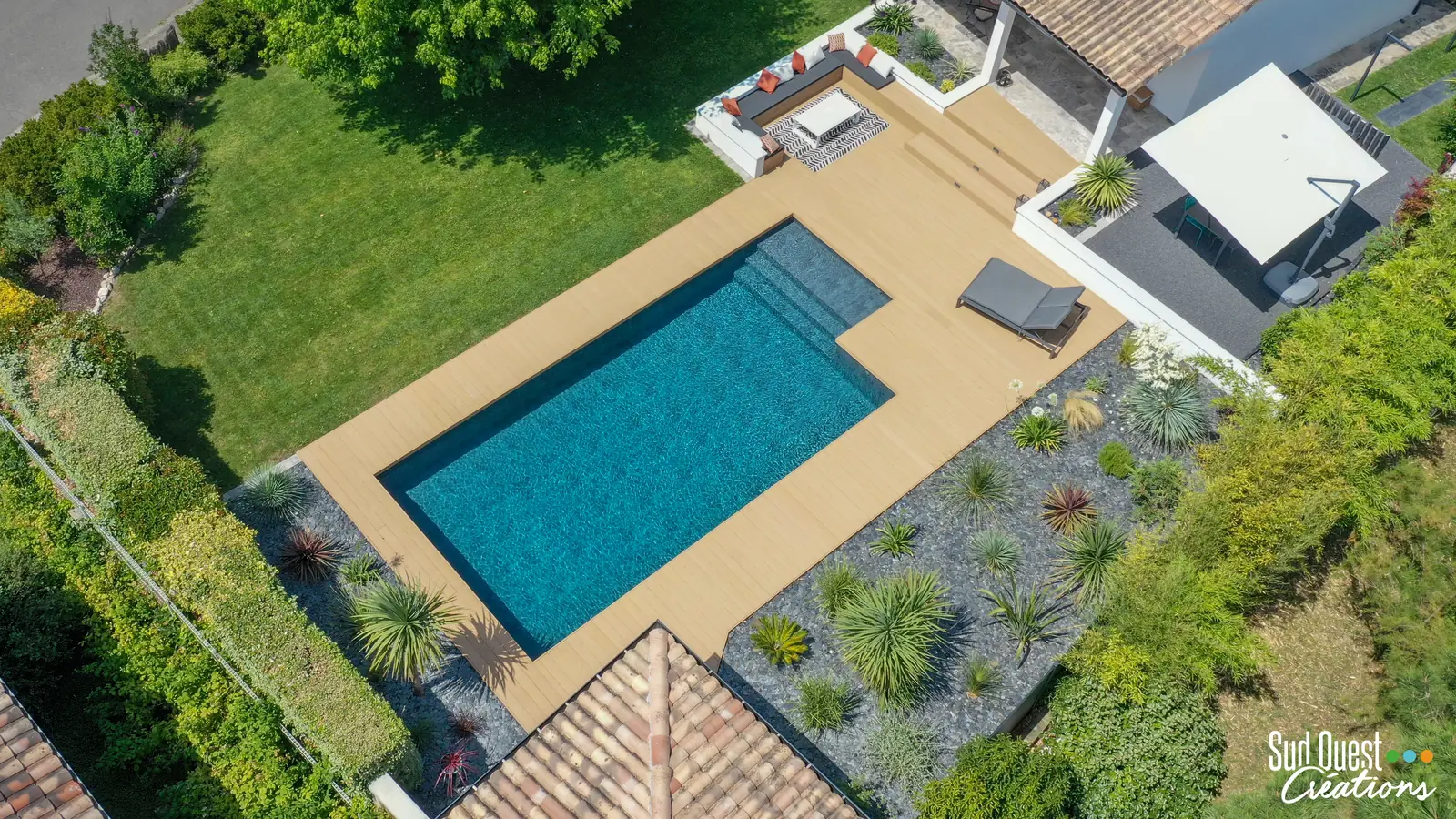Vue zénithale d'une piscine avec terrasse composite, salon encastré et massifs exotiques