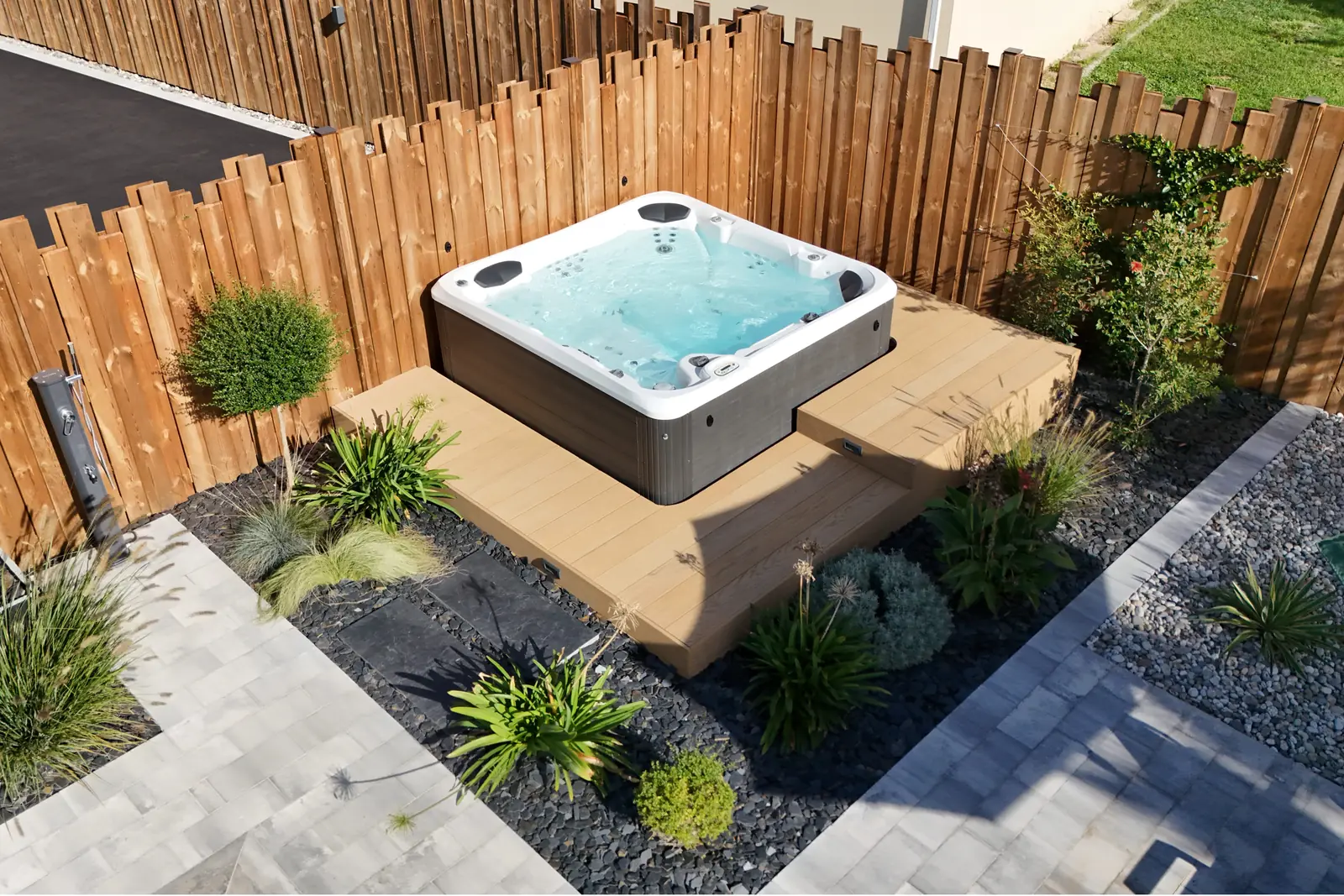 Spa encastré dans une terrasse bois, entouré de massifs et d'une clôture en bois