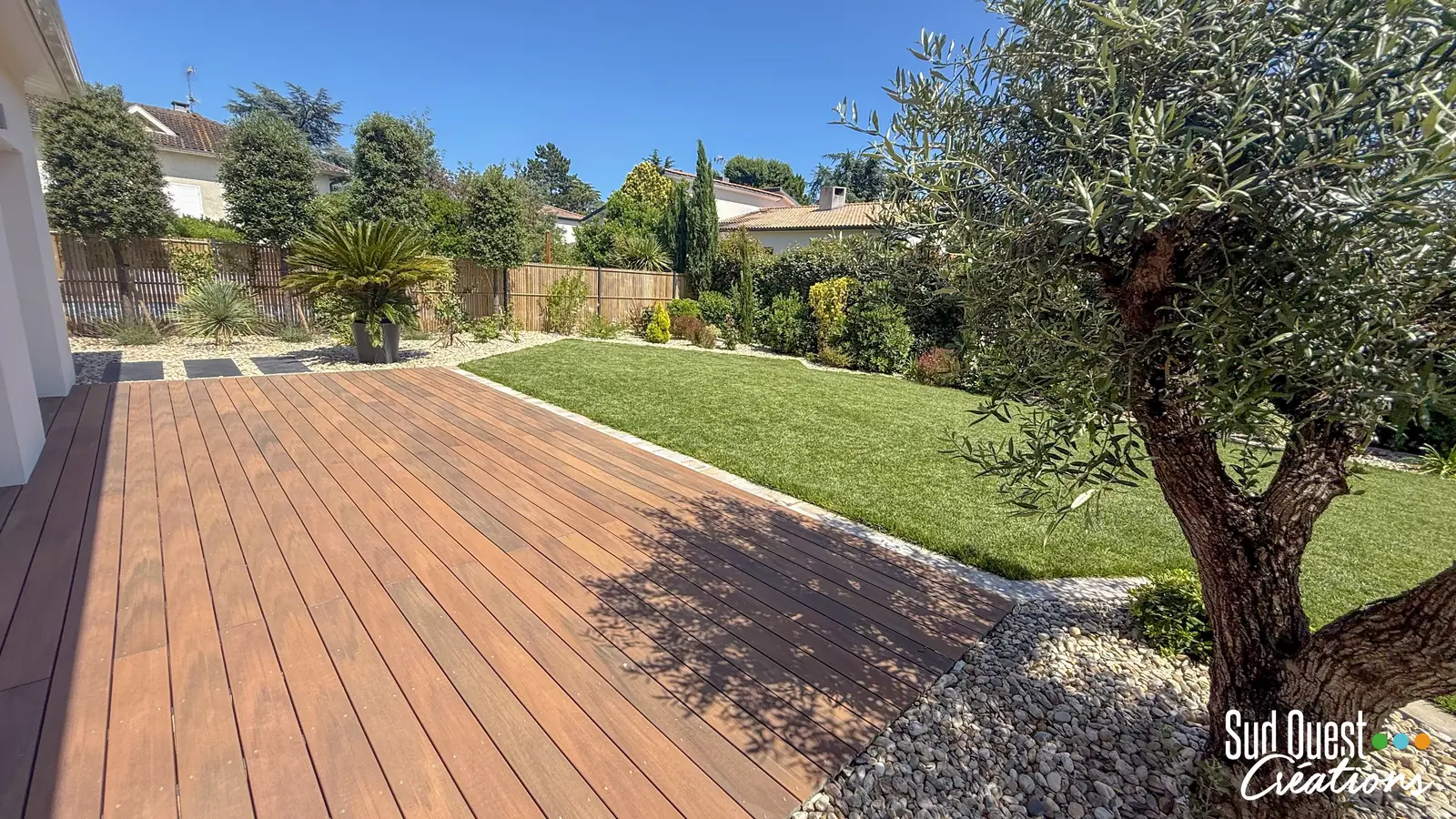 Terrasse en bois exotique bordant une pelouse et un olivier dans un jardin près de Toulouse