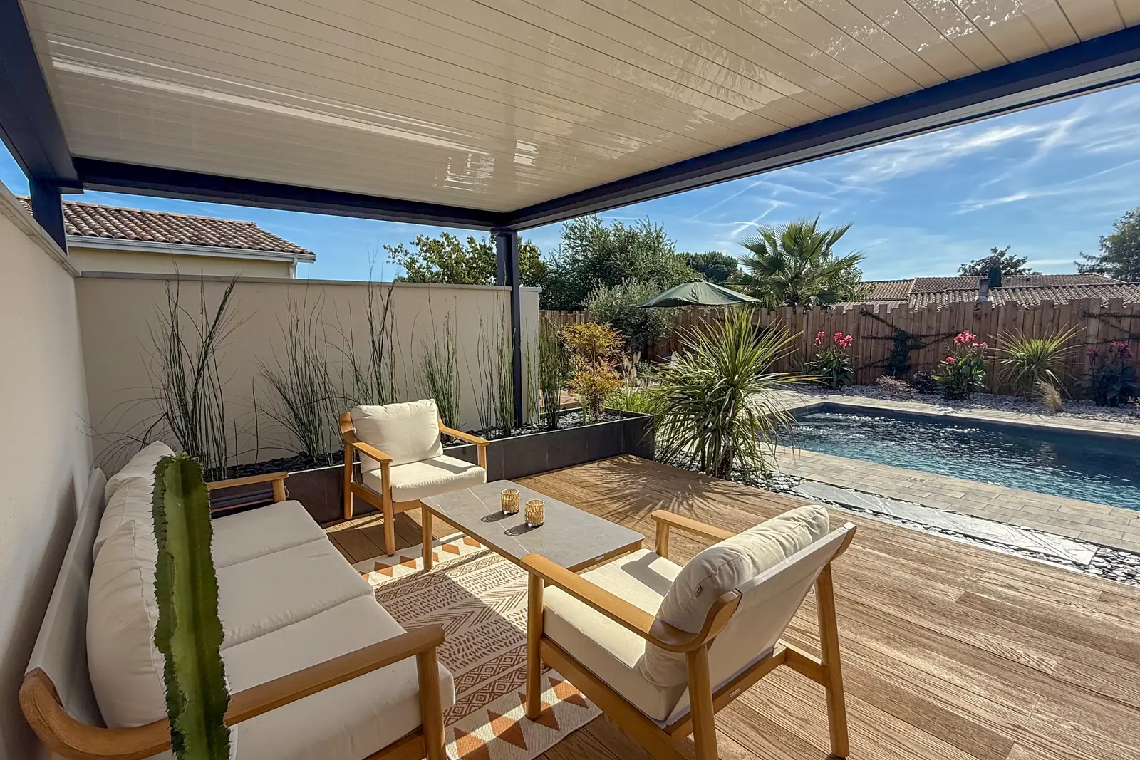 Salon extérieur sur terrasse bois sous pergola bioclimatique, avec vue sur la piscine