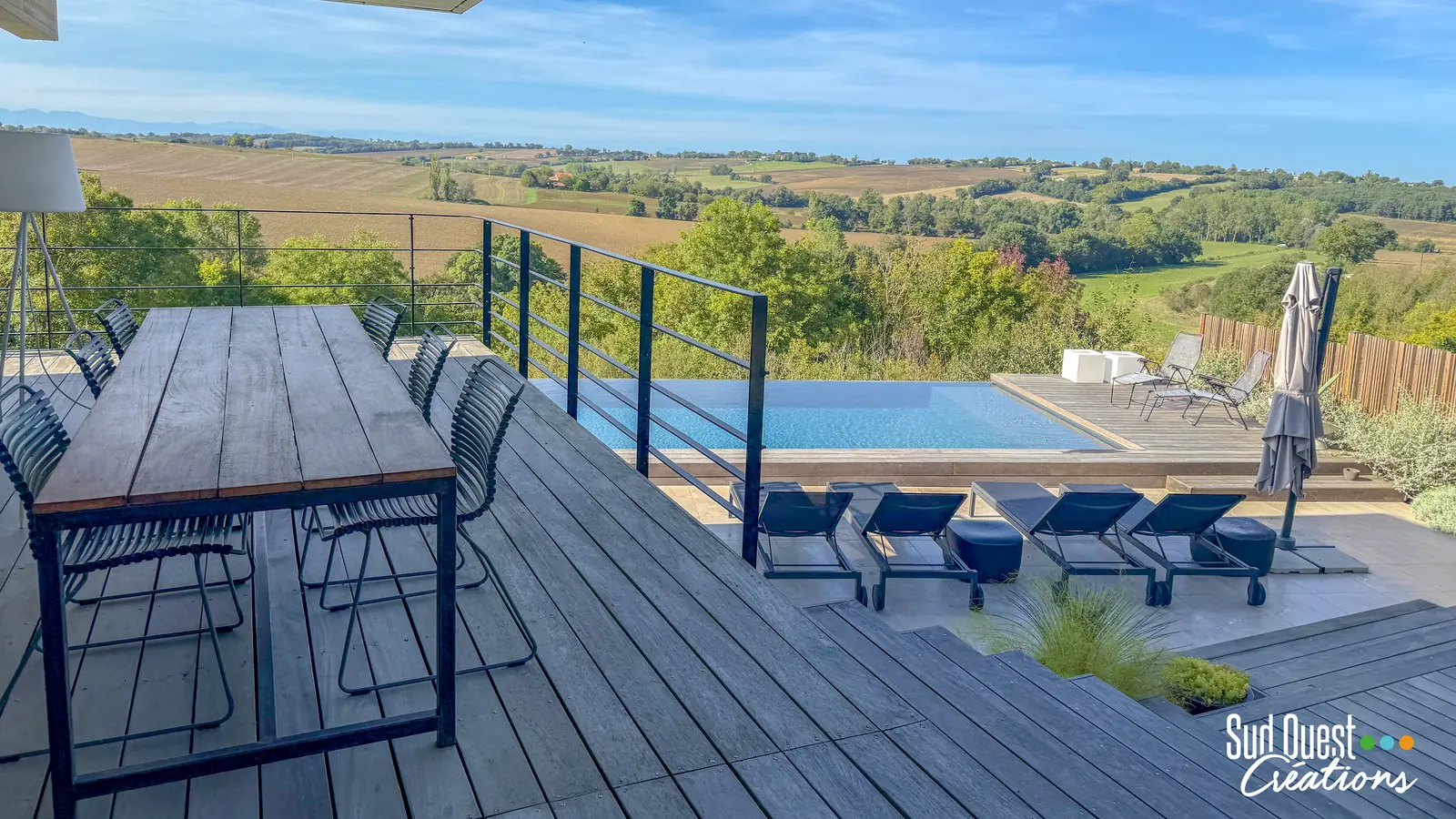 Terrasse en bois avec table de repas surplombant une piscine à débordement face à la campagne