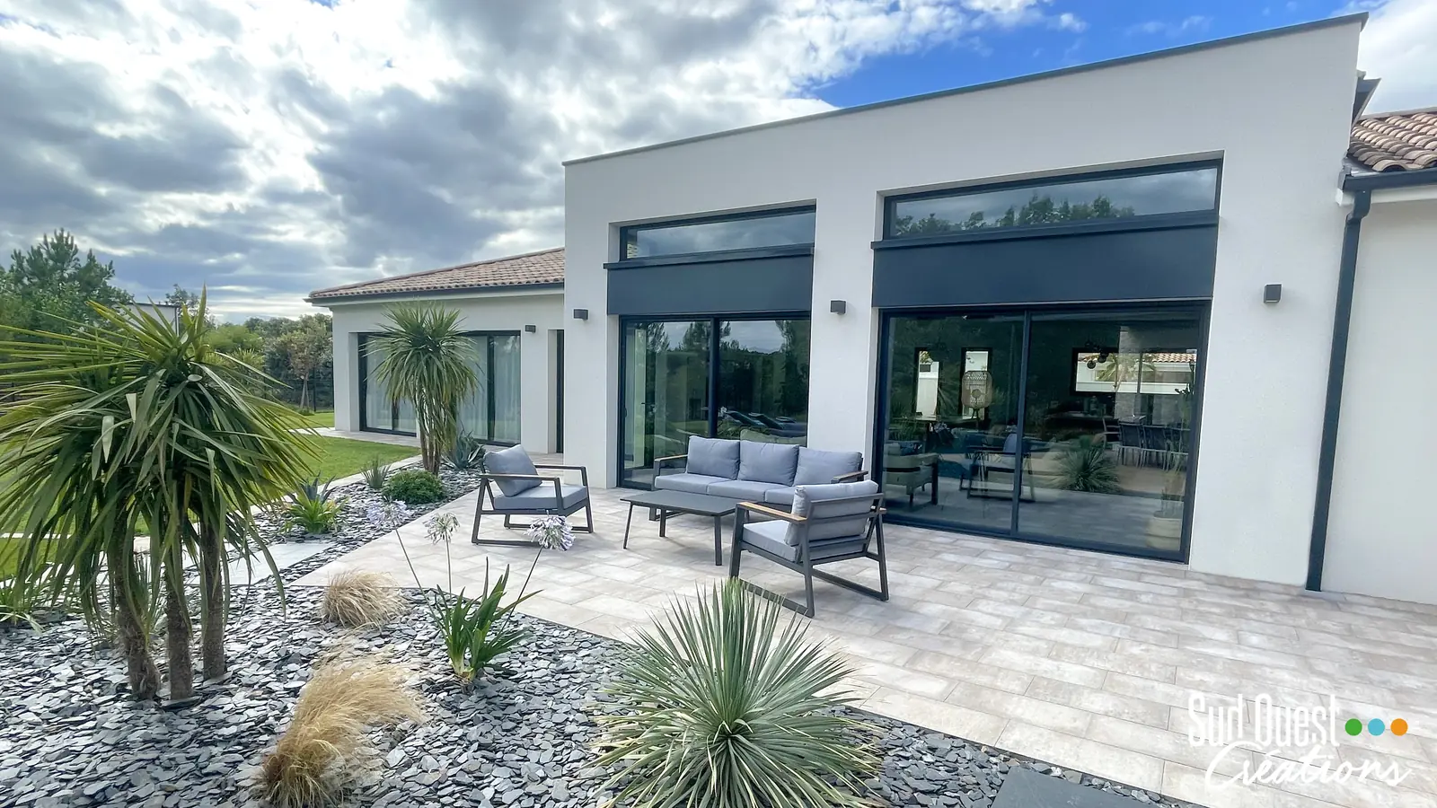 Terrasse en dallage avec salon extérieur, massifs d'ardoise, yuccas et agapanthes